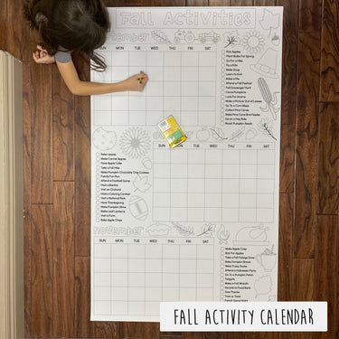 A large coloring banner titled 'FALL ACTIVITY CALENDAR' laid out on a table with a child coloring it.